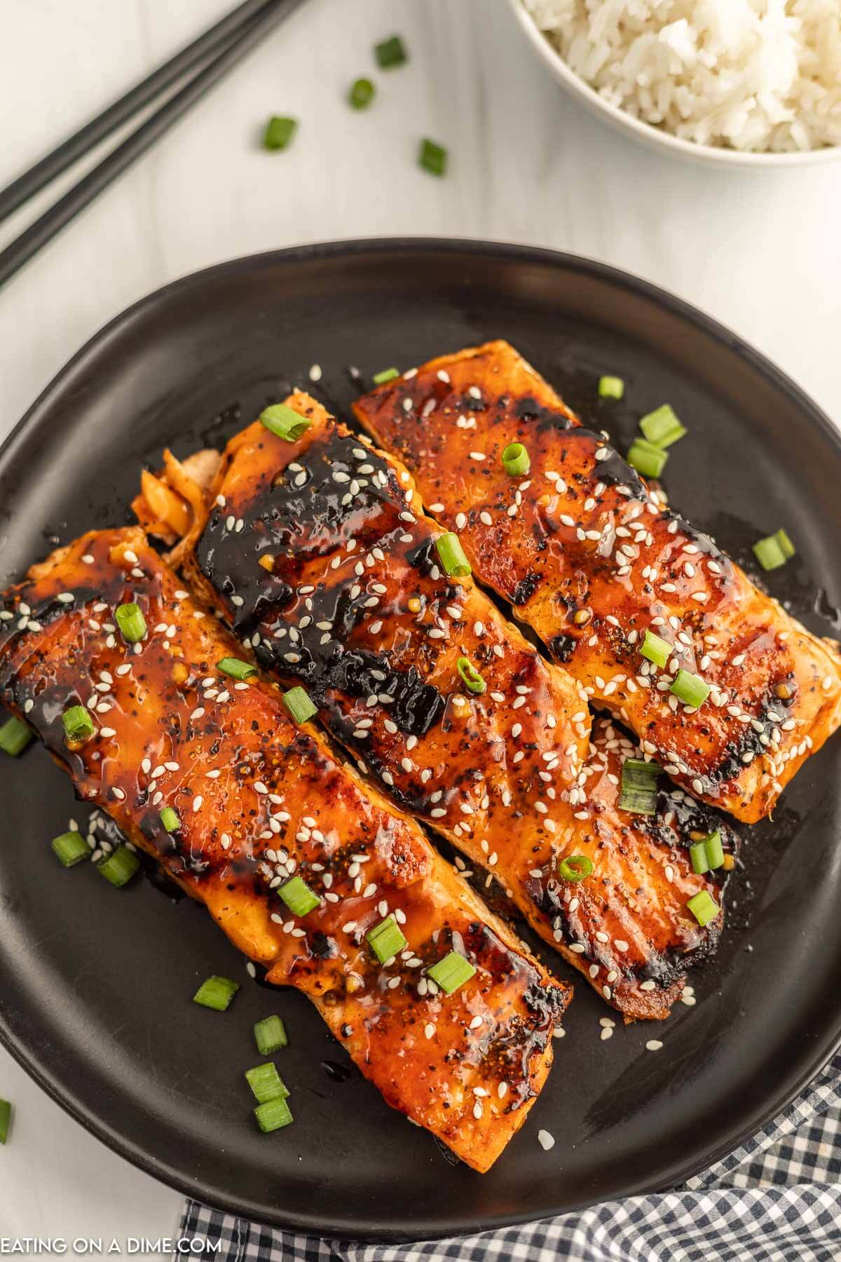 Teriyaki Salmon on a black plate topped with sesame seeds and diced green onions. 