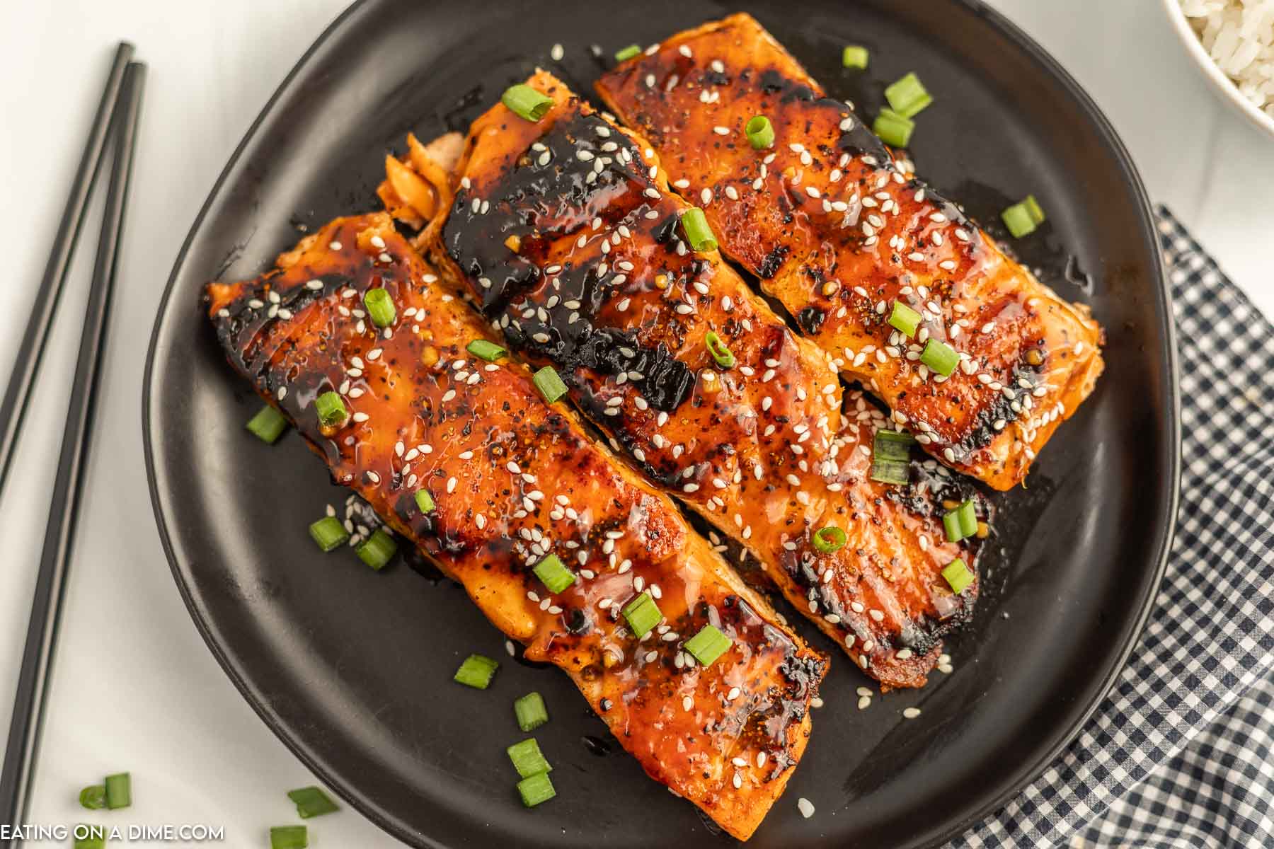 Teriyaki Salmon on a black plate topped with sesame seeds and diced green onions. 