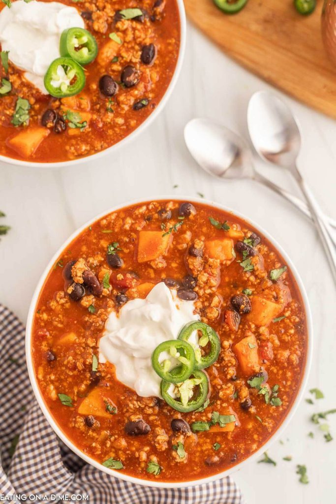 Close up image of turkey sweet potato chili in a white bowl topped with sour cream and slice jalapenos
