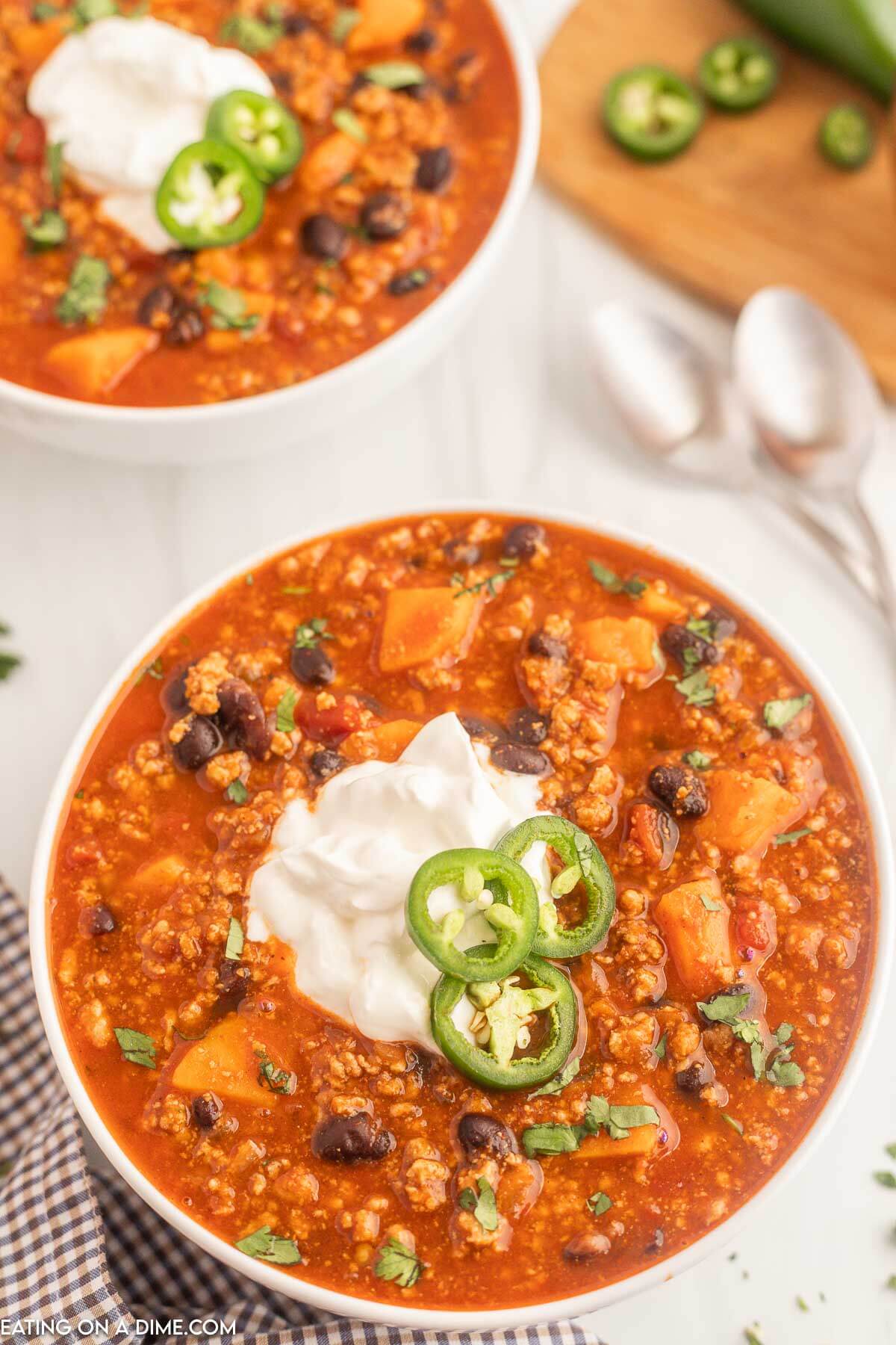 Close up image of turkey sweet potato chili in a white bowl topped with sour cream and slice jalapenos