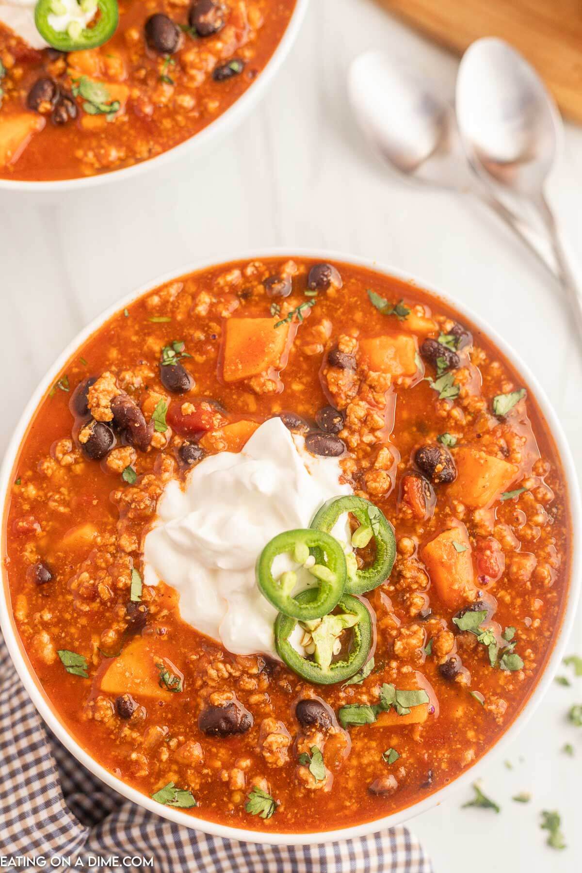 Close up image of turkey sweet potato chili in a white bowl topped with sour cream and slice jalapenos
