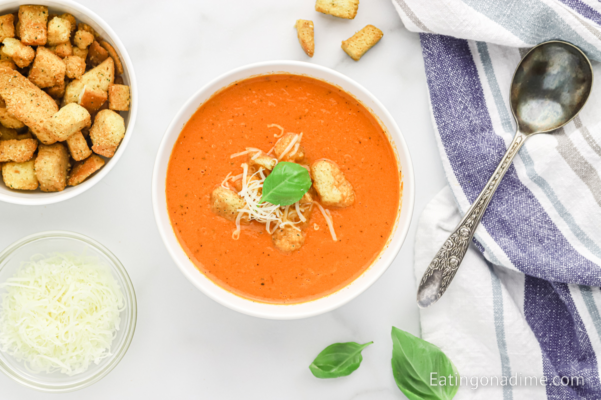 A bowl of tomato soup topped with croutons, fresh basil and cheese