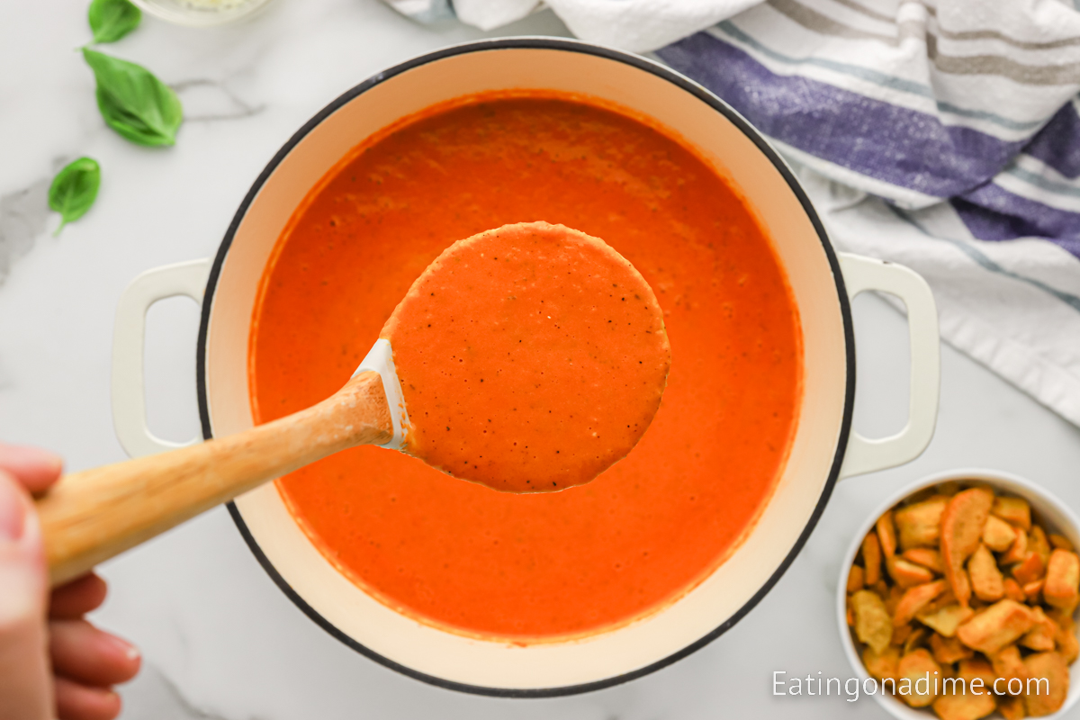A Dutch Oven full of tomato soup with a serving on a spoon