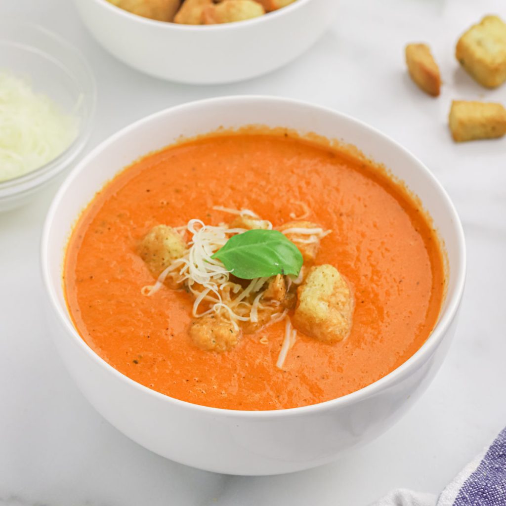 A bowl of tomato soup topped with croutons, fresh basil and cheese