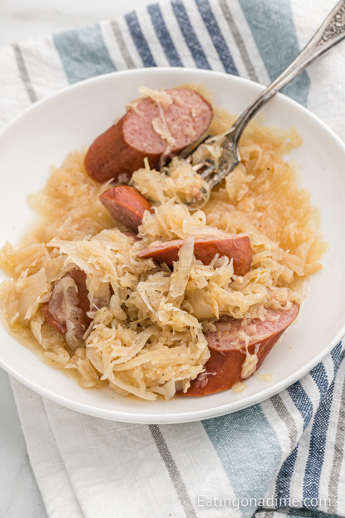 Sauerkraut and slice sausage on a white plate with a fork