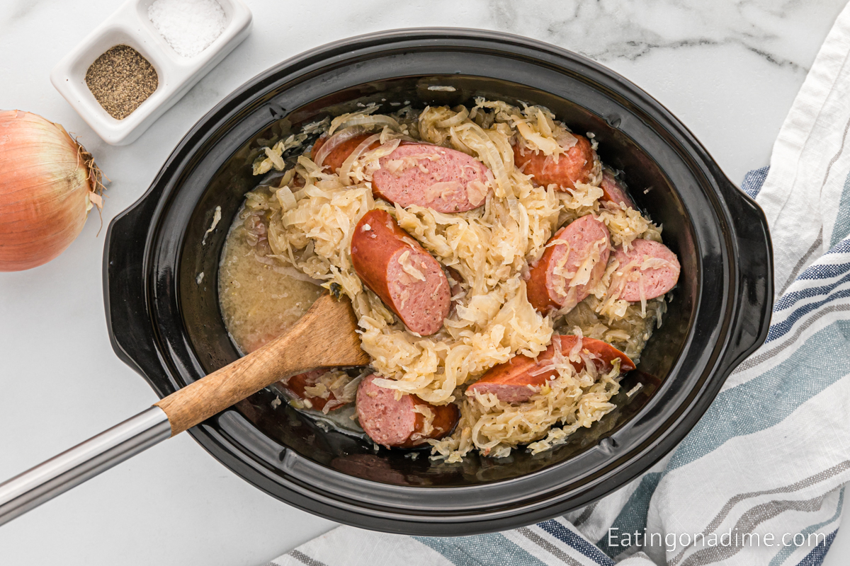 Sauerkraut and slice sausage in the crock pot with a wooden spoon