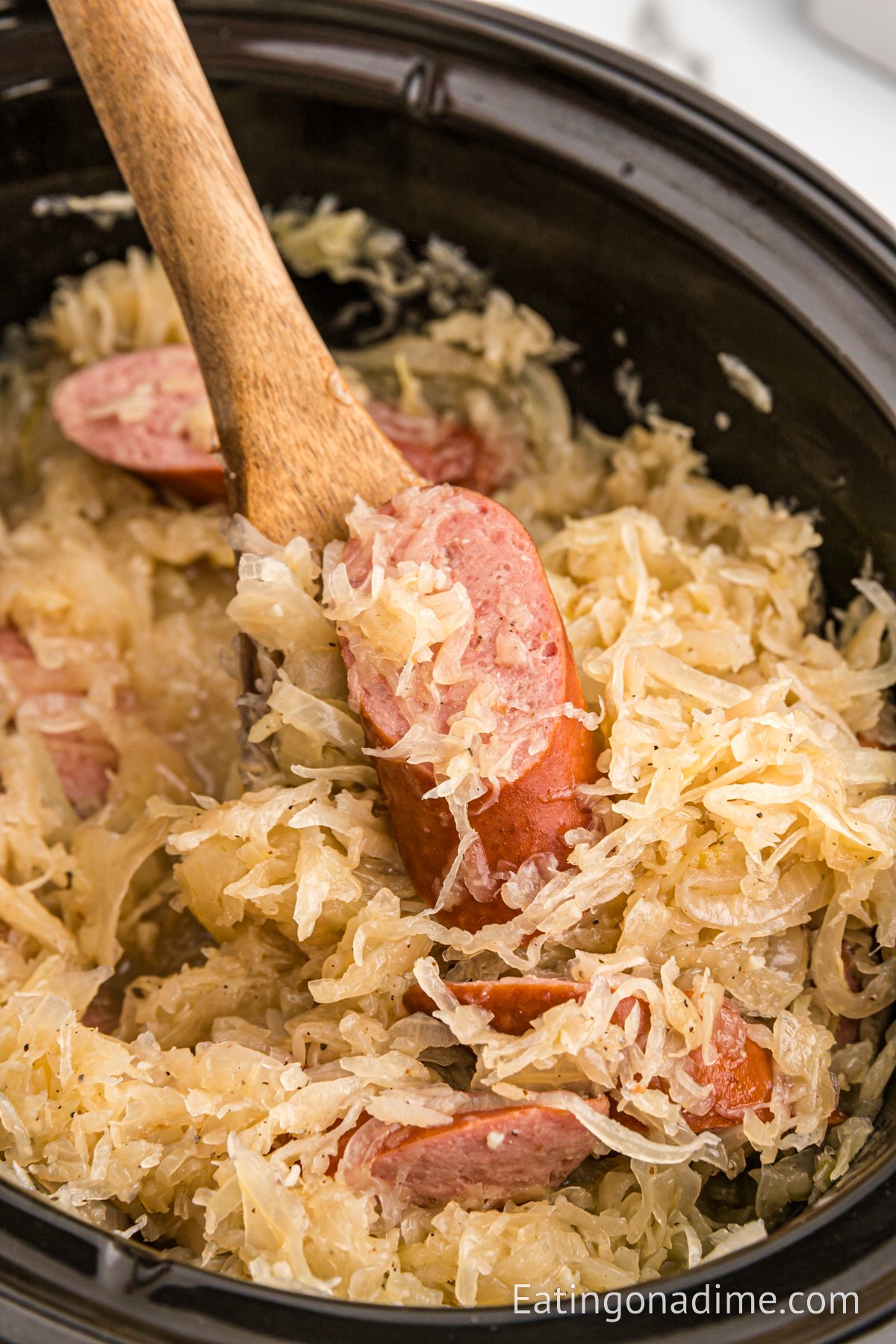 Sauerkraut and slice sausage in the crock pot with a wooden spoon