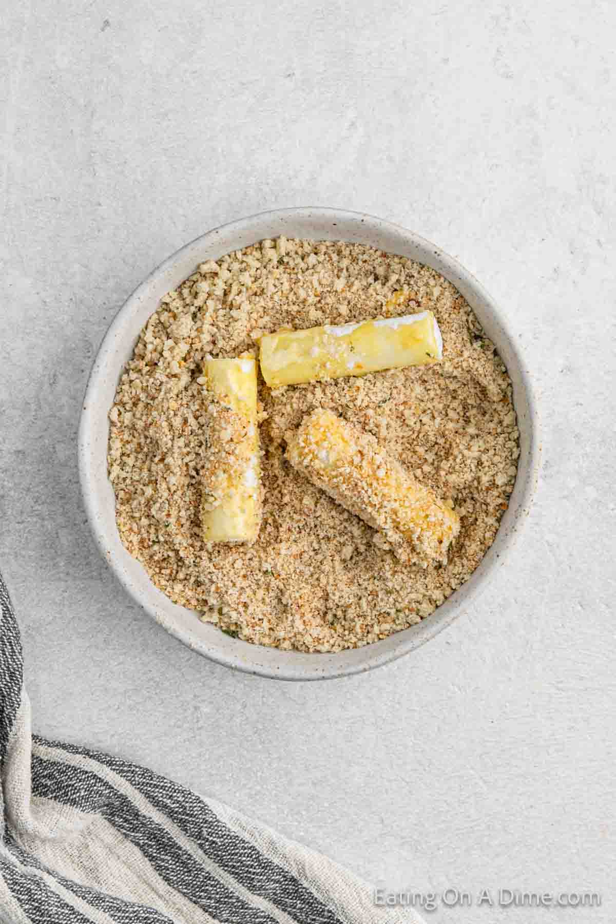 Rolling the cheese sticks in egg, flour, and bread crumb mixture