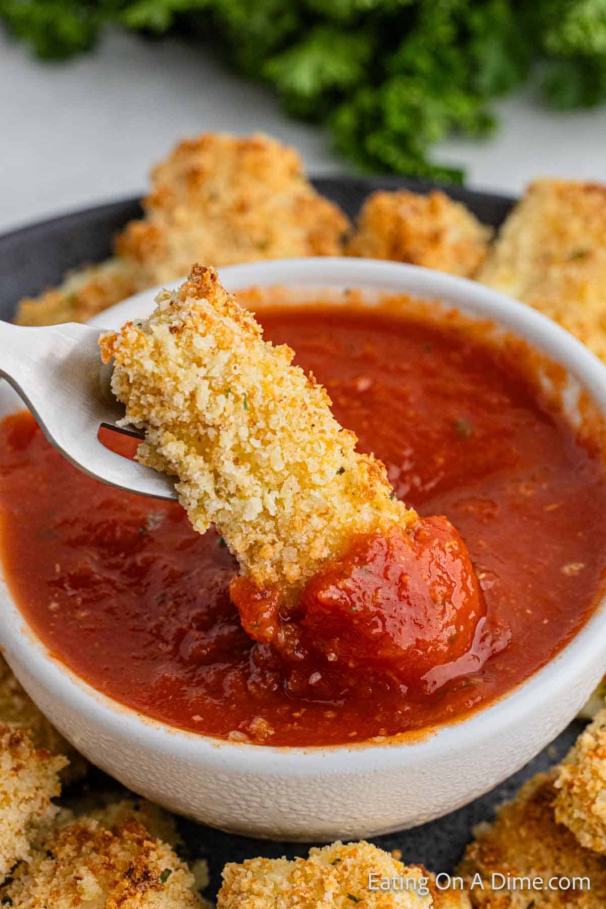 Dipping cheese sticks on pizza sauce with a fork