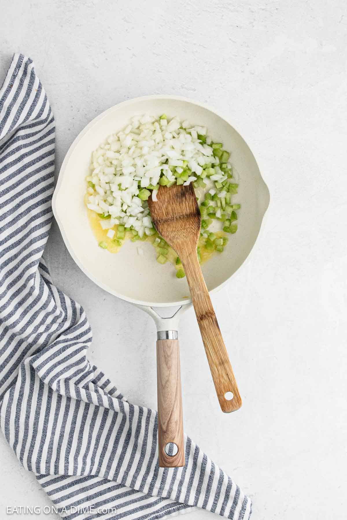 Chopped onion and celery in a skillet with a wooden spoon.
