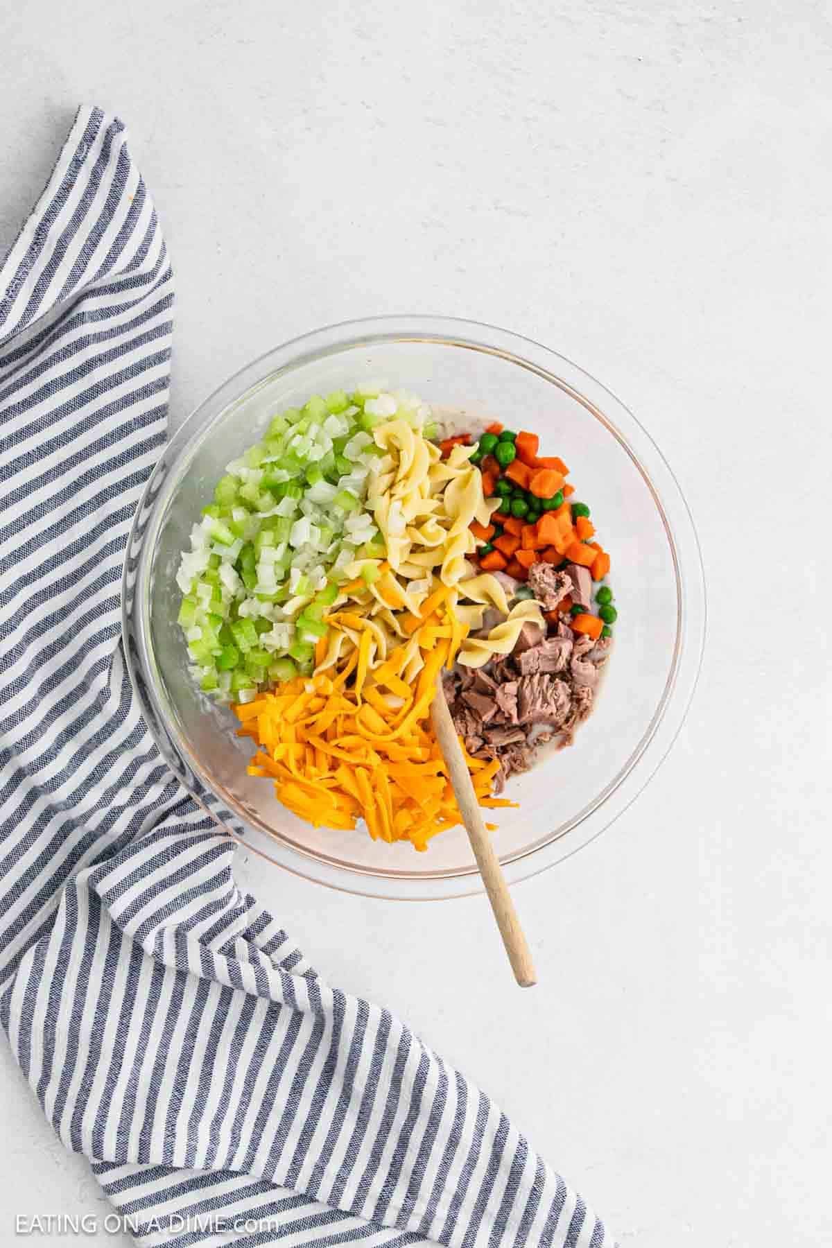 Shredded cheese, chopped veggies, egg noodles, and tuna combined in a bowl.
