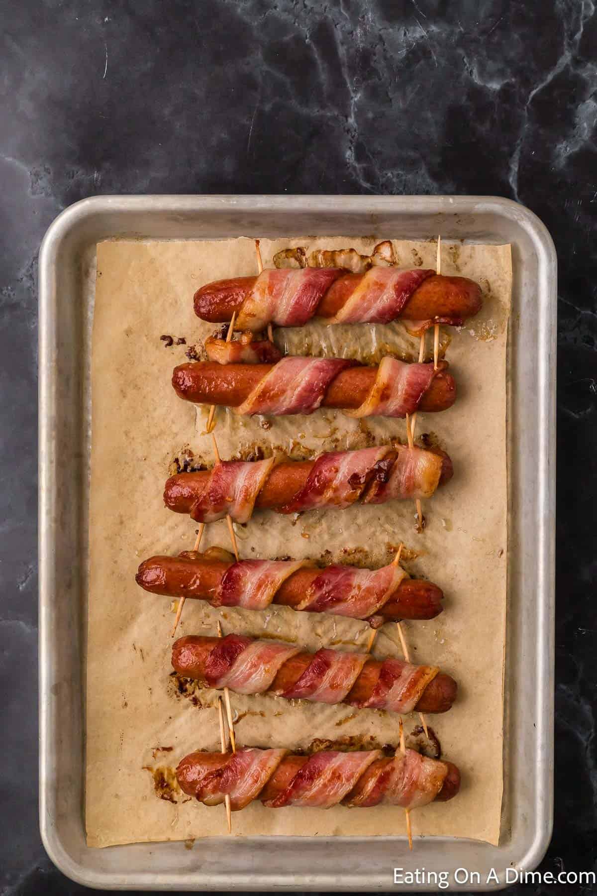Cooked bacon wrapped hot dogs on a baking sheet