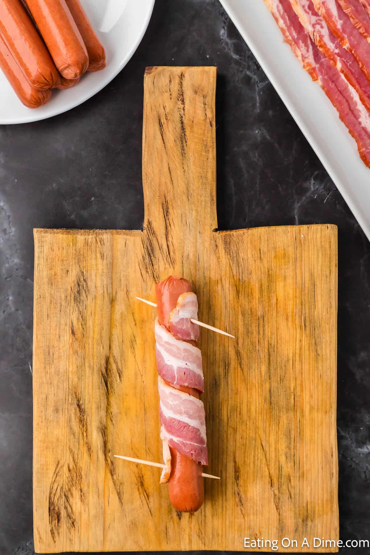 Wrapping a slice of bacon around a hot dogs and securing with toothpicks