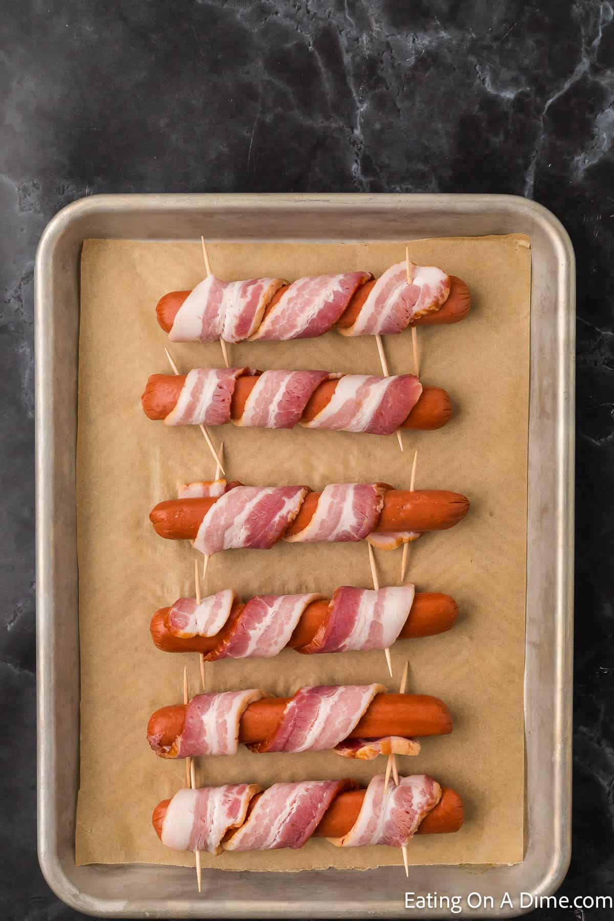 Placing the bacon wrapped hot dogs on a baking sheet lined with parchment paper