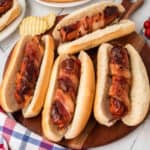 Bacon wrapped hot dogs on a wooden cutting board.