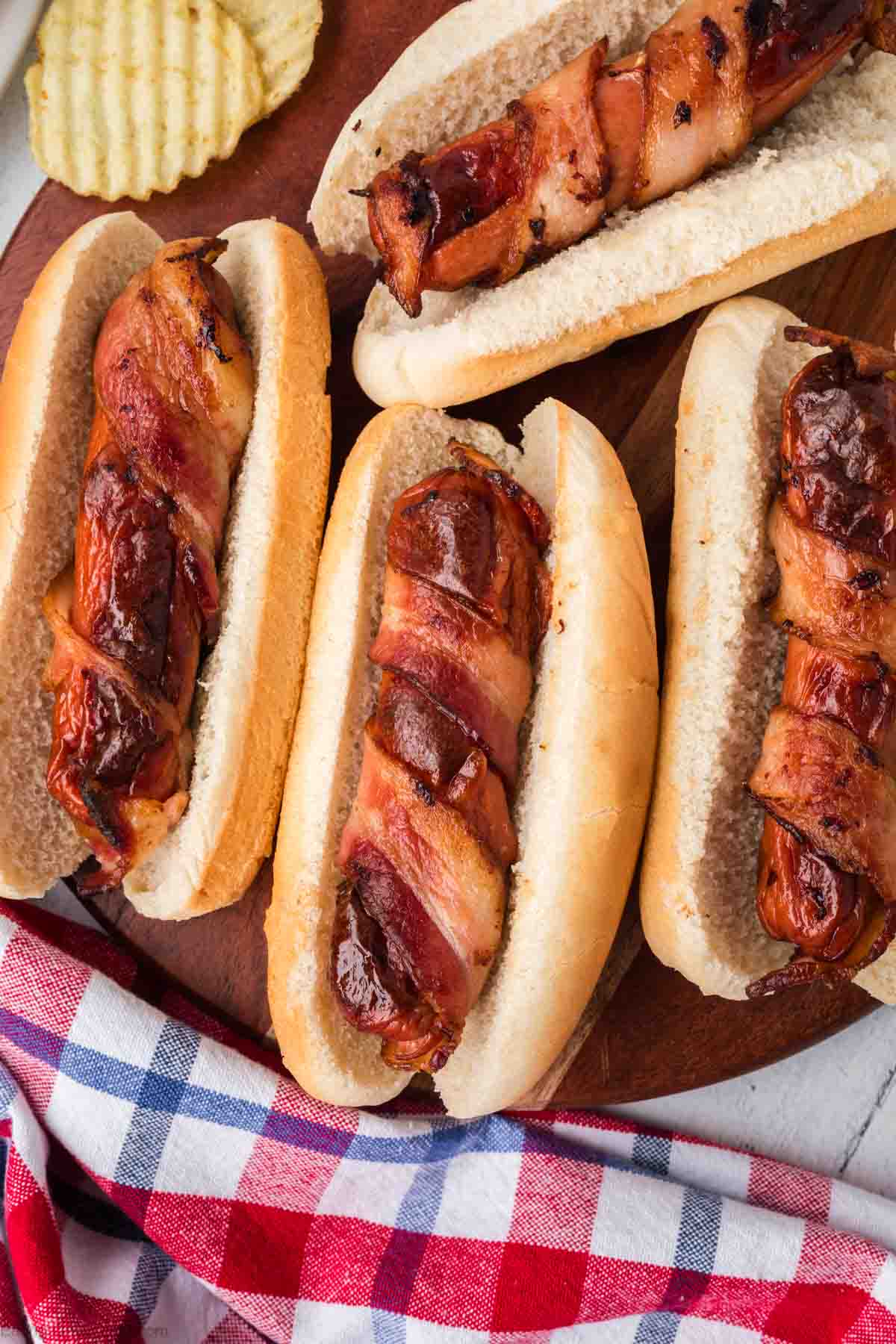 Bacon Wrapped hot dogs in a hot dog buns on a wooden platter