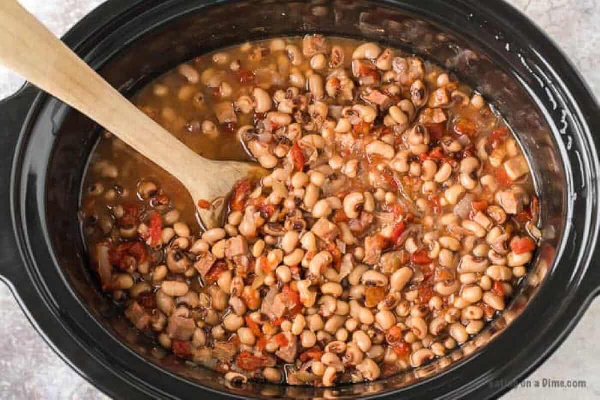 A Crock Pot Black Eyed Peas dish filled with tender black-eyed peas, diced tomatoes, and savory seasonings, all mixed together and stirred gently with a wooden spoon.