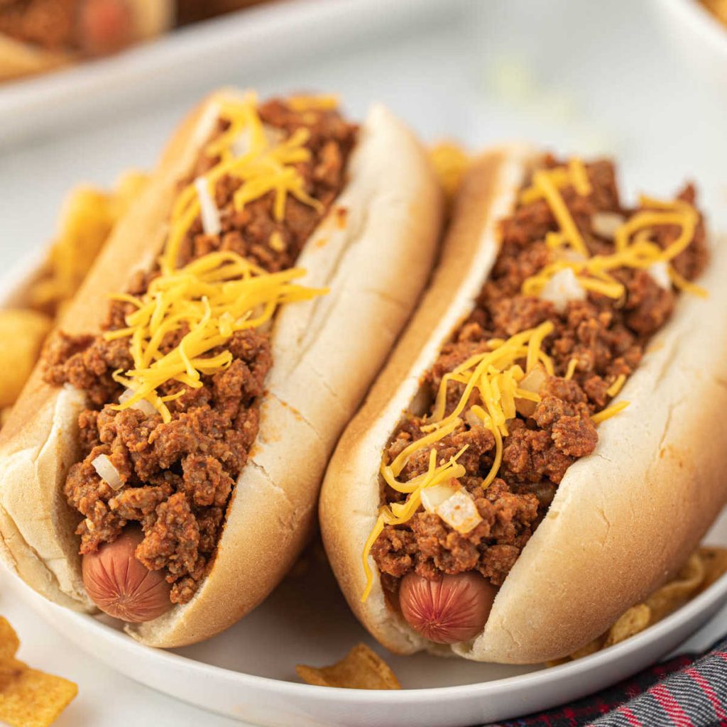 Hot dogs topped with chili, cheese, and onions on a plate