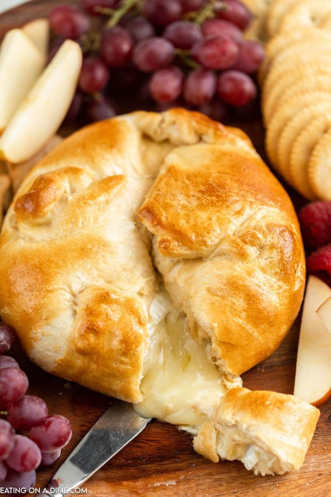 Baked Brie in crescent roll on a platter with a side of fruit and crackers