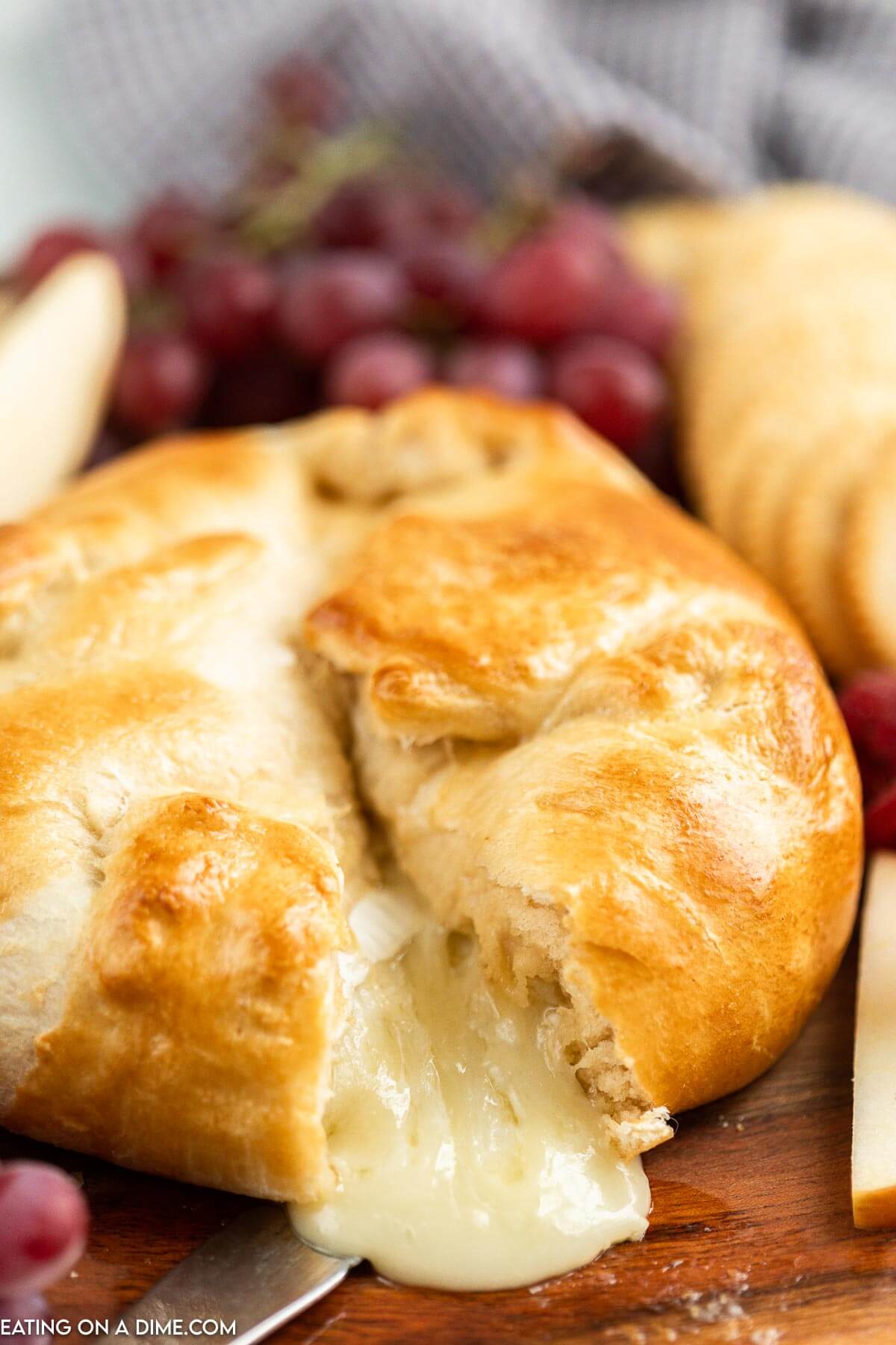 Baked Brie in crescent roll on a platter with a side of fruit and crackers