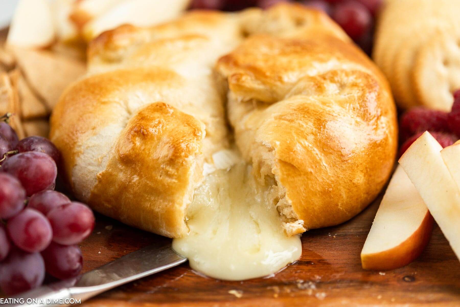 Baked Brie in crescent roll on a platter with a side of fruit and crackers