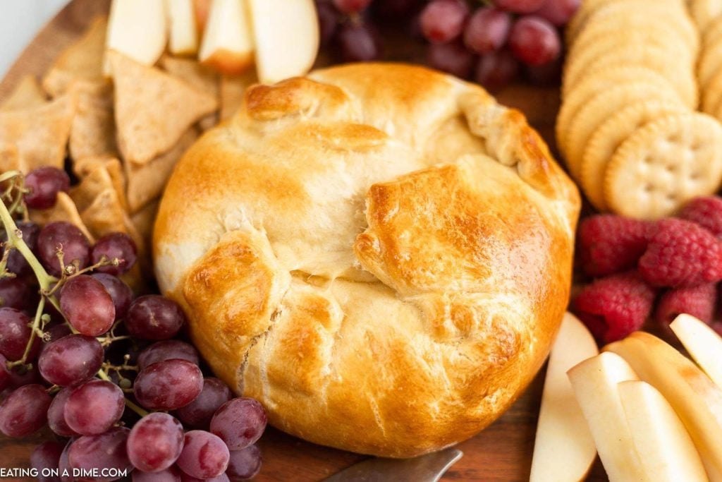 Baked Brie in crescent roll on a platter with a side of fruit and crackers