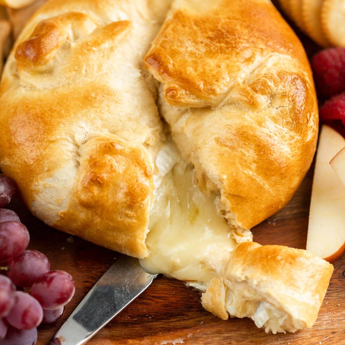 Baked Brie in crescent roll on a platter with a side of fruit and crackers