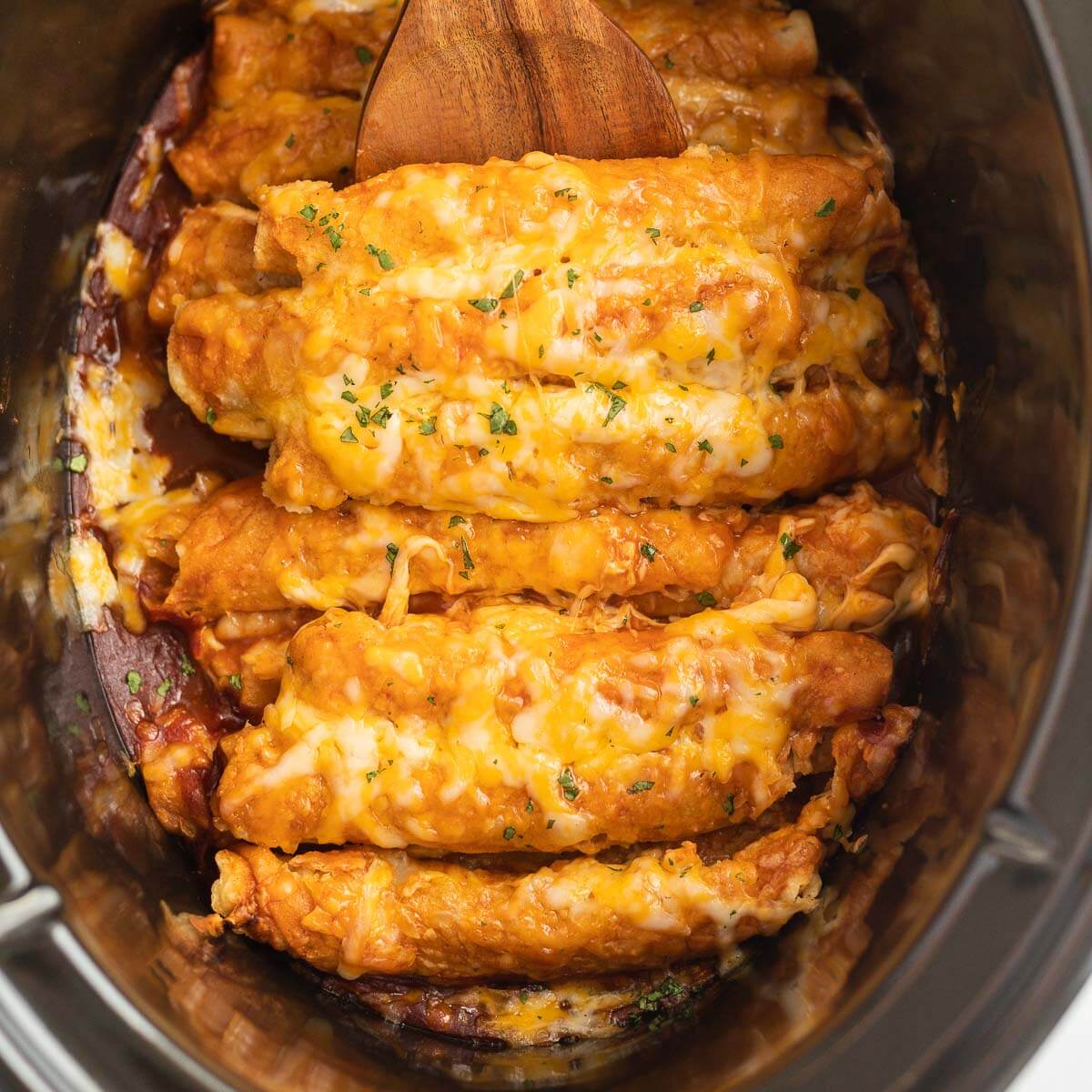 Lazy Enchiladas in a slow cooker with a wooden spoon