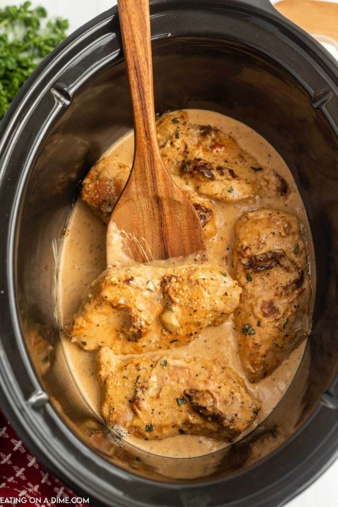 Marry Me Chicken in the slow cooker with a wooden spoon