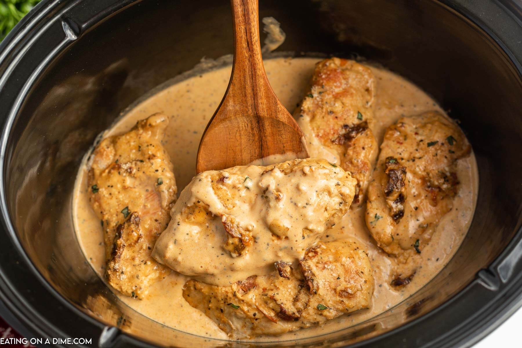 Marry Me Chicken in the slow cooker with a wooden spoon