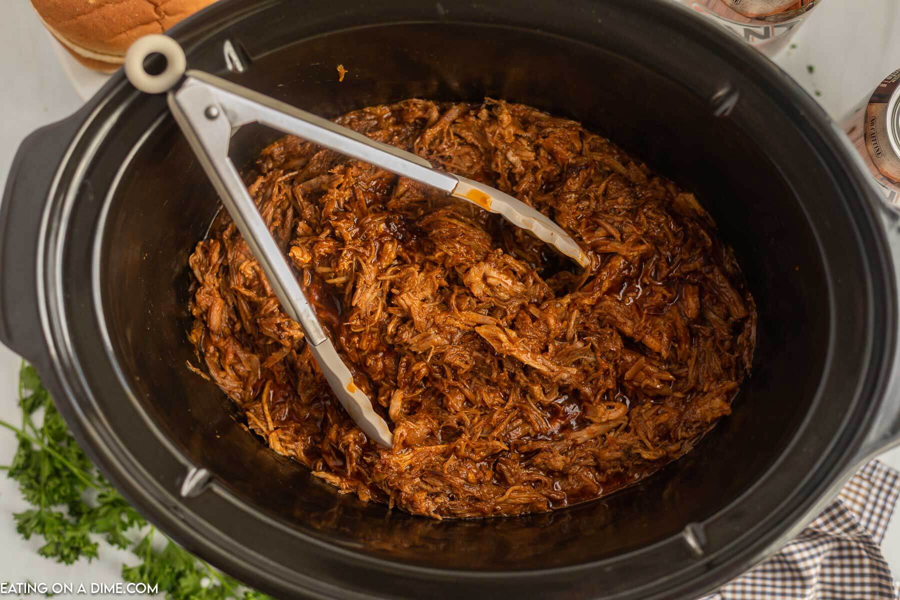 Shredded BBQ Pork in a slow cooker with silver tongs