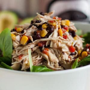 A close-up of a bowl filled with shredded chicken mixed with black beans, corn, and diced tomatoes, served on a bed of fresh spinach leaves. The salad is colorful and healthy, ideal for a meal.