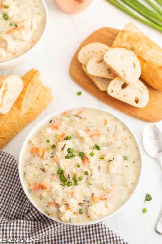 Panera Chicken and Wild Rice soup in a bowl with a spoon with loafs of french bread