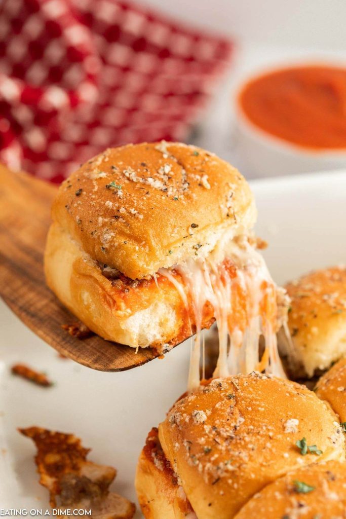 Hawaiian Roll Pizza Sliders in a baking dish and a slider being served on a wooden spatula