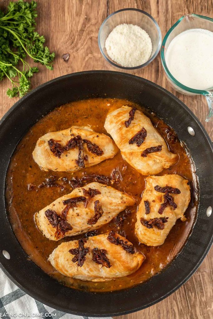 Adding the sundried tomatoes to the chicken in a skillet with sauce
