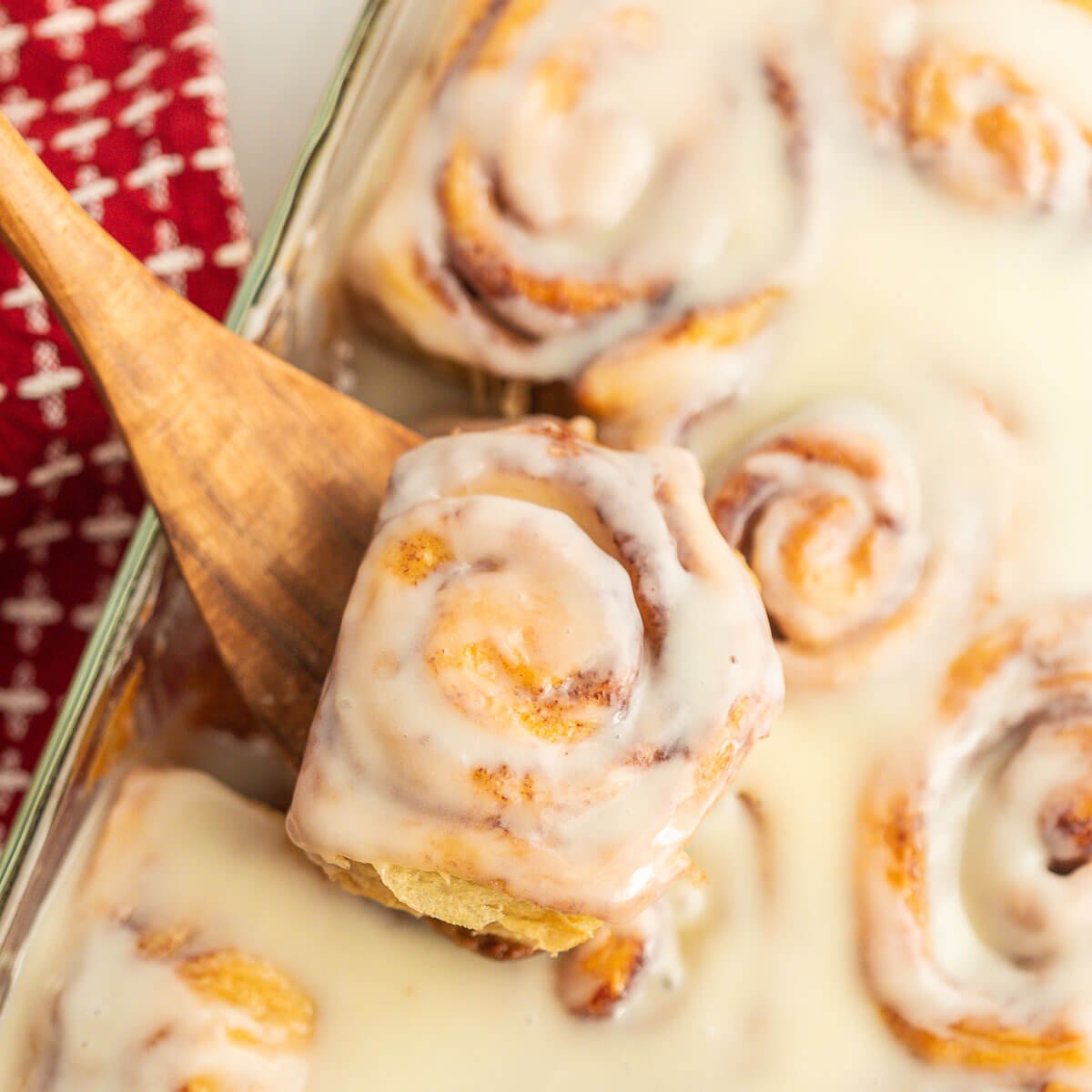 Cinnamon Rolls in a baking dish with a serving on a wooden spoon