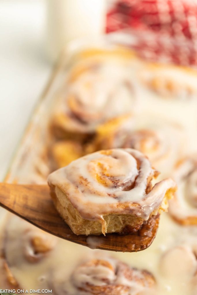 Cinnamon Rolls in a baking dish with a serving on a wooden spoon