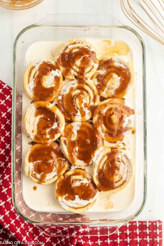 Uncooked cinnamon rolls in a baking dish covered with heavy cream and the cinnamon mixture