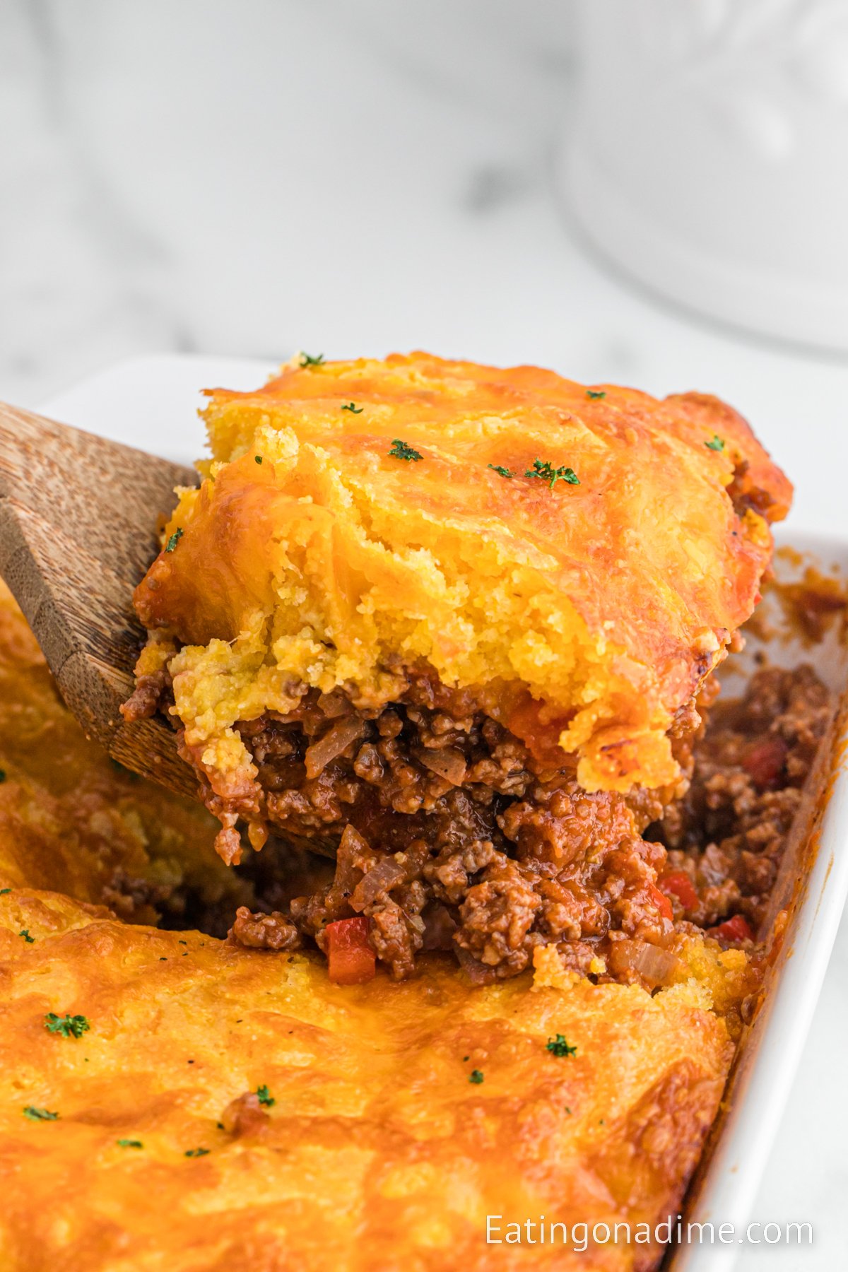 Sloppy Joe Cornbread Casserole in a 8x8 baking dish with a serving on a wooden spatula