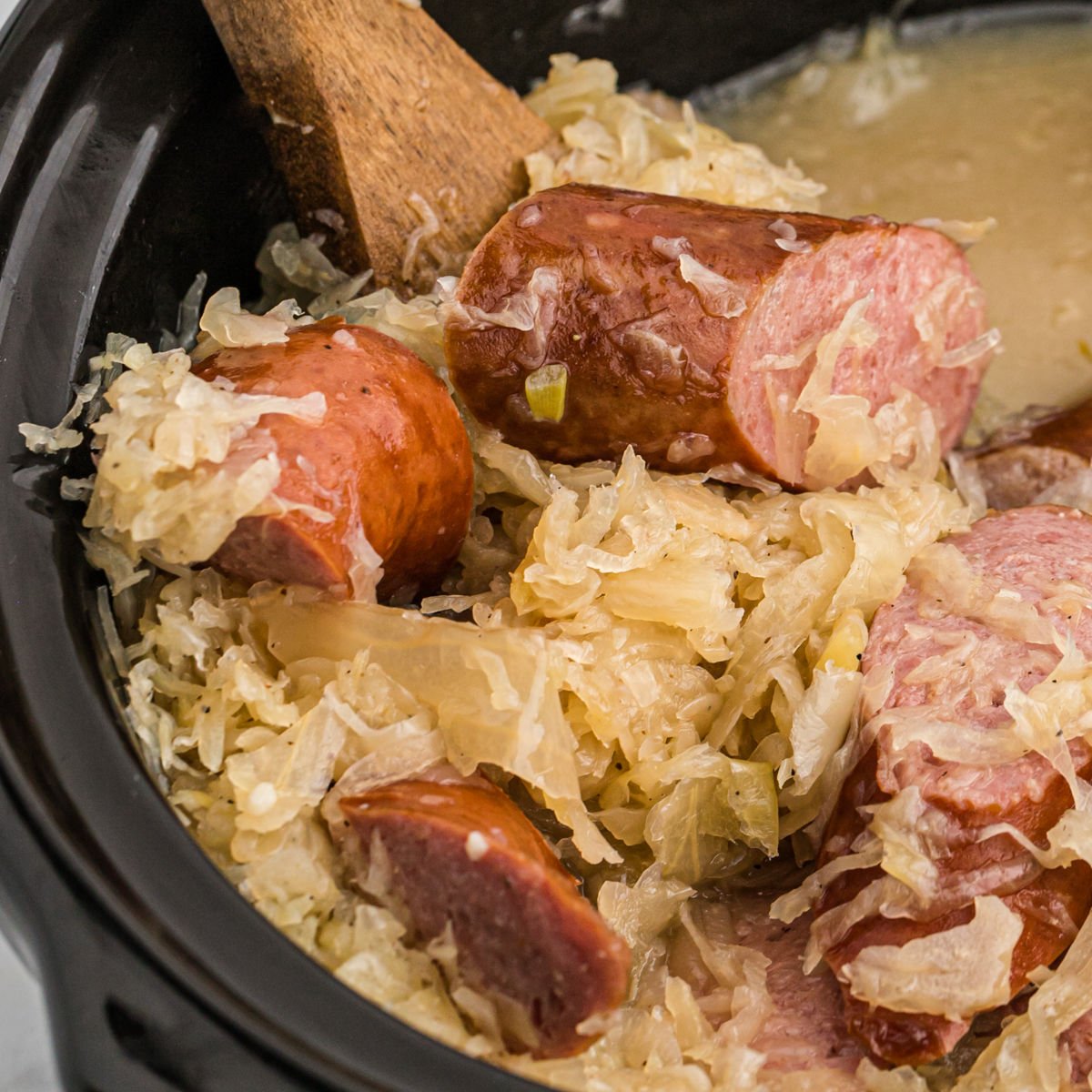 Sauerkraut and slice sausage in the crock pot with a wooden spoon