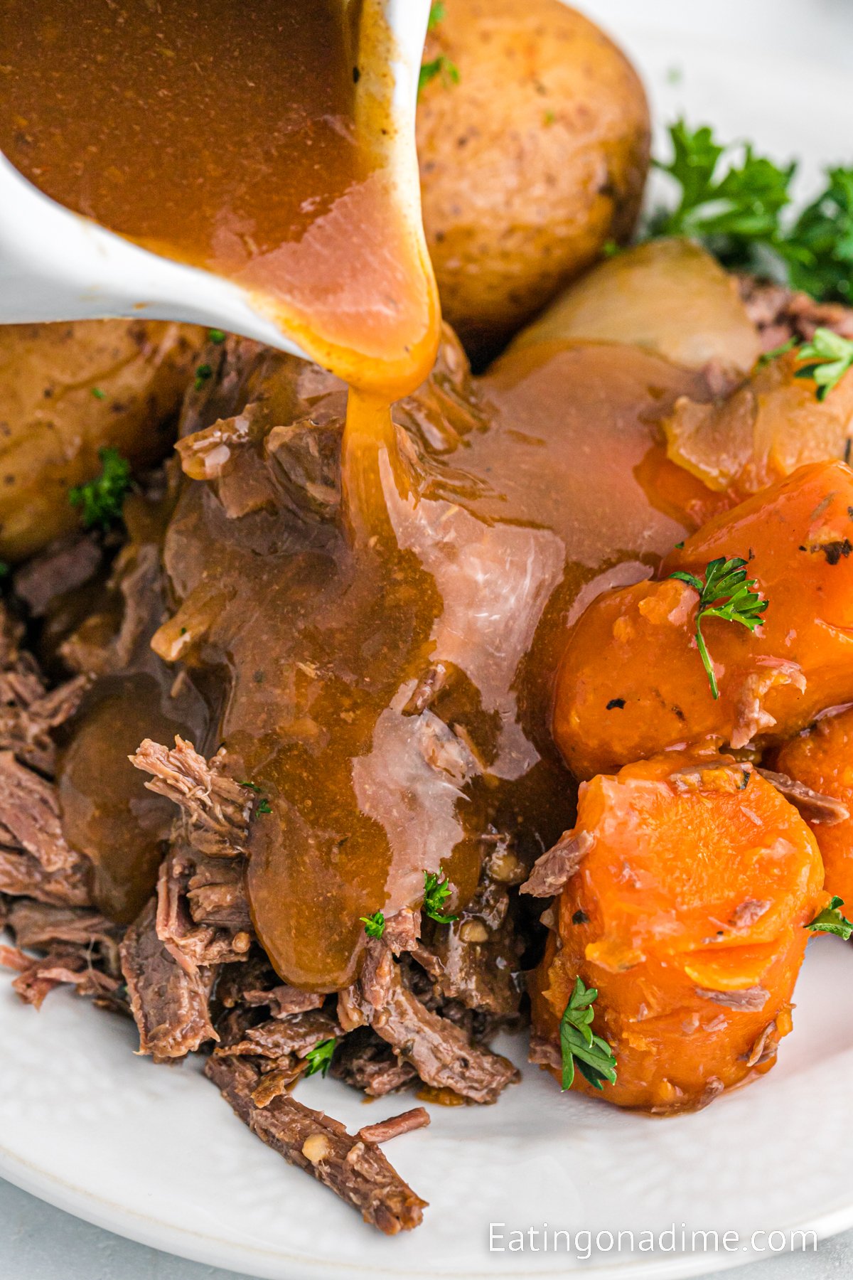 Venison Roast potatoes and carrots on a platter with gravy being poured over