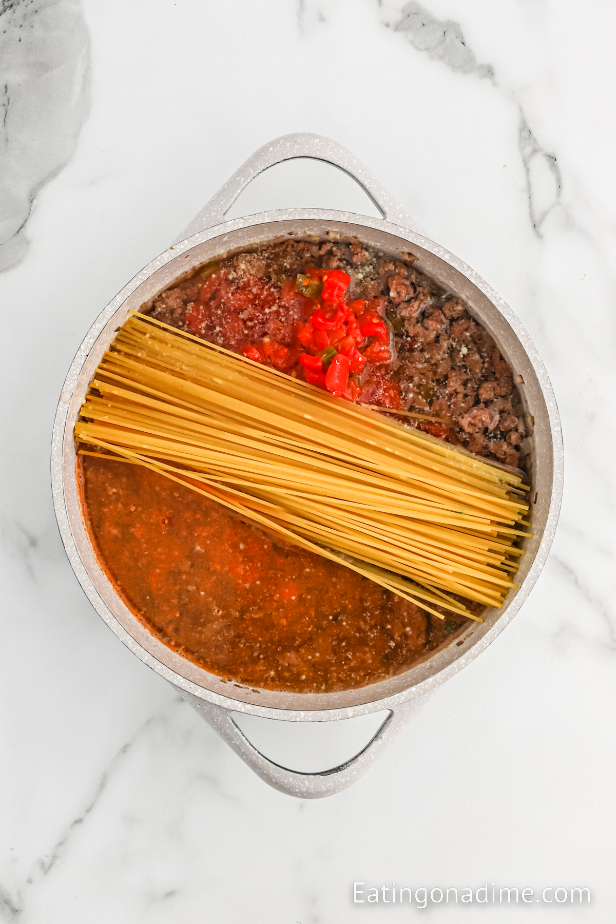 Spaghetti noodles in a large pot with cook ground beef diced tomatoes and broth