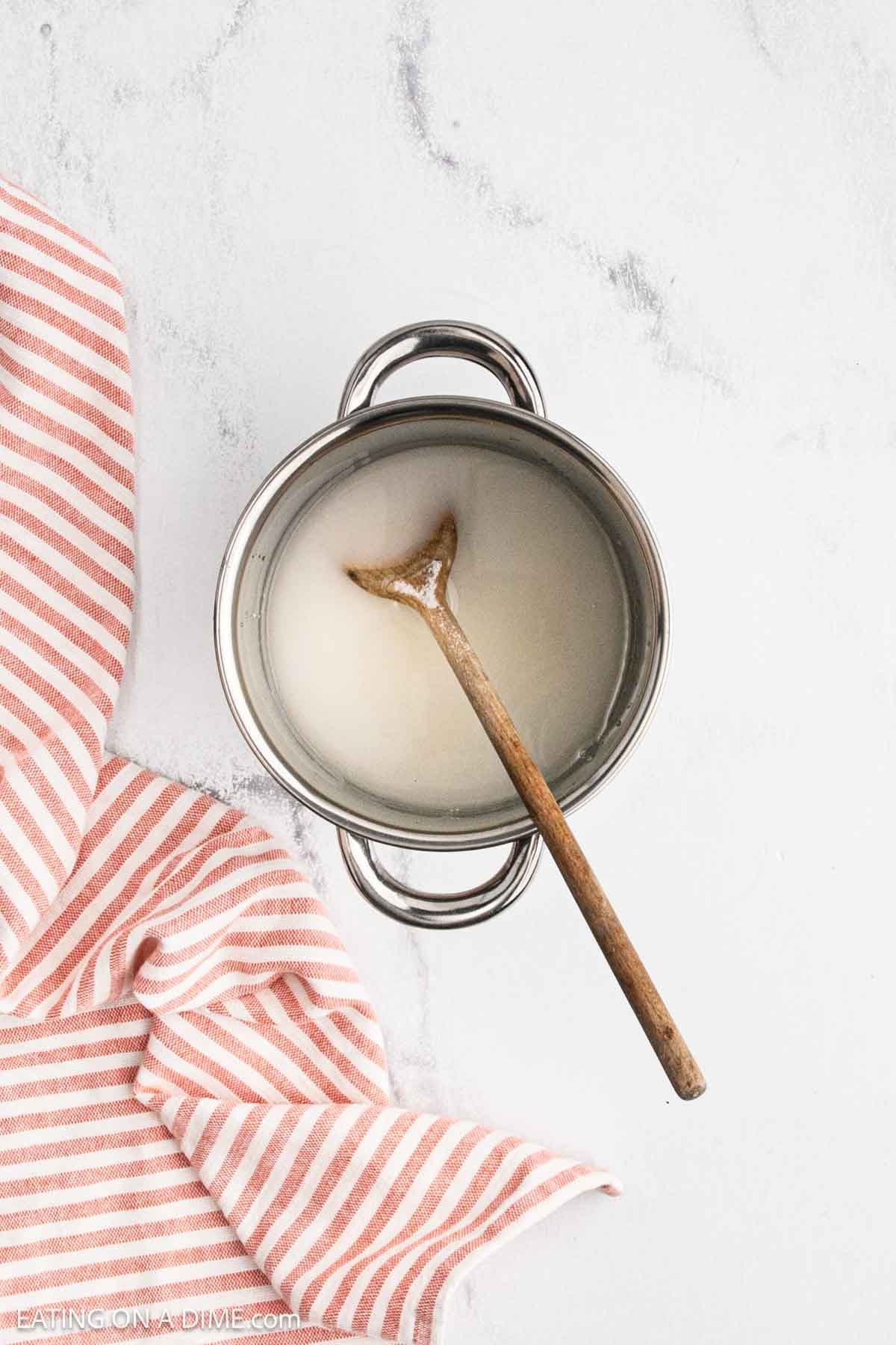 Sugar and water mixed together in a saucepan with a wooden spoon.