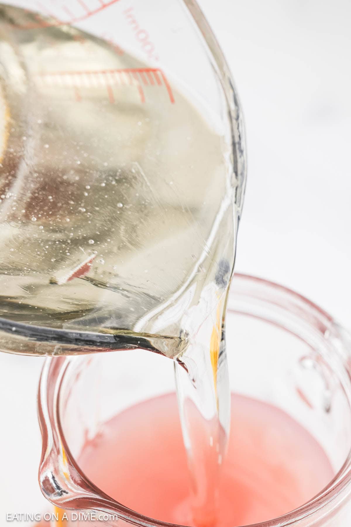 Pouring simple syrup and juices together in a clear glass pitcher.