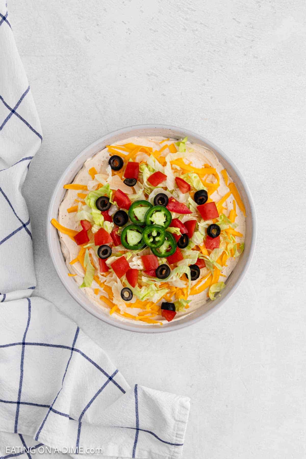 Slice jalapenos, diced tomatoes, slice black olives, lettuce, and shredded cheese topped the cream cheese mixture in the serving dish