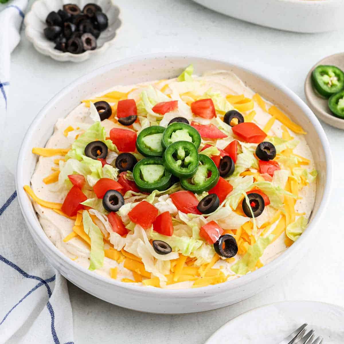 Taco dip topped with slice jalapenos, black olives, diced tomatoes, shredded cheese and lettuce 