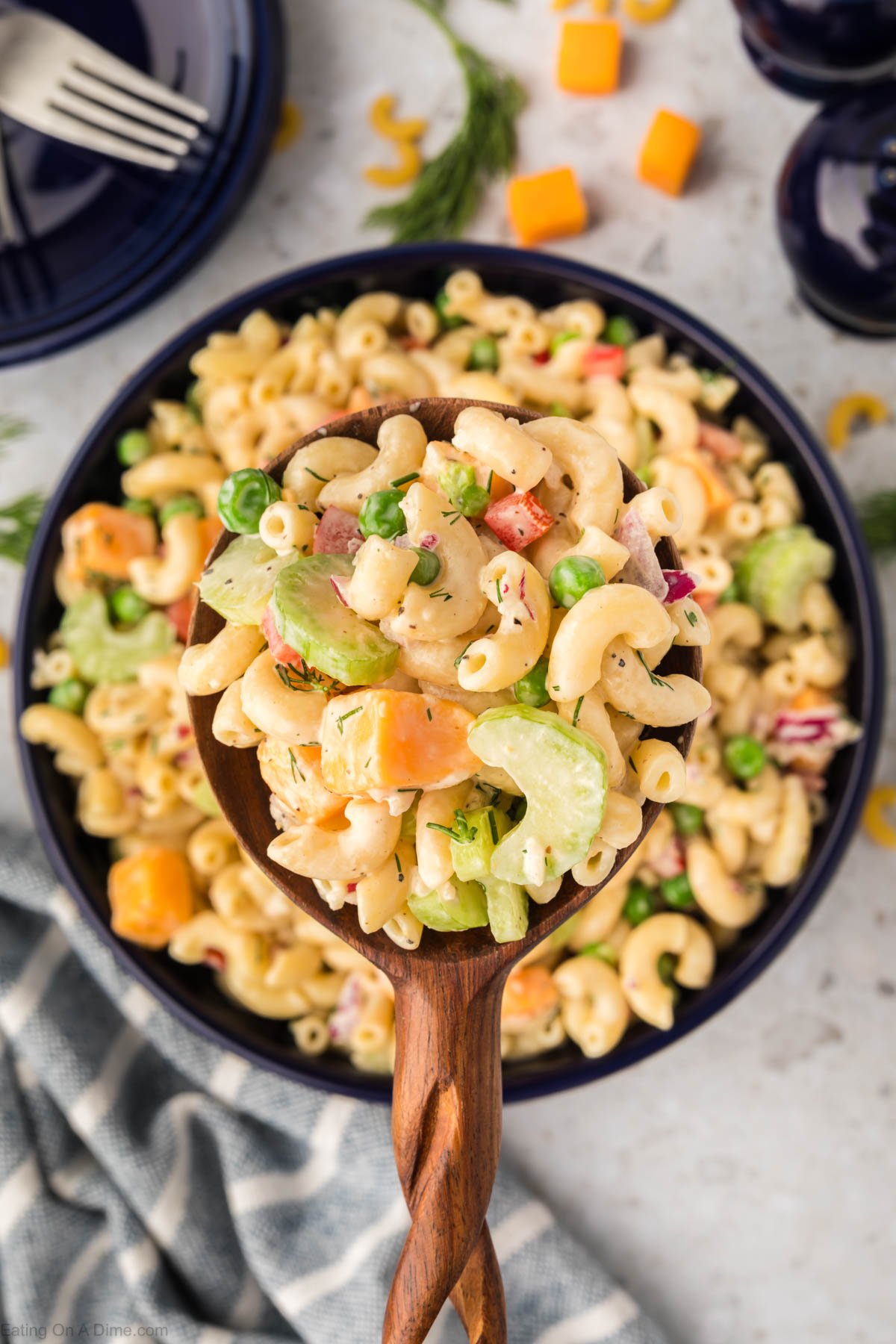 A large spoonful of macaroni salad being scooped out of a large bowl of macaroni salad. 