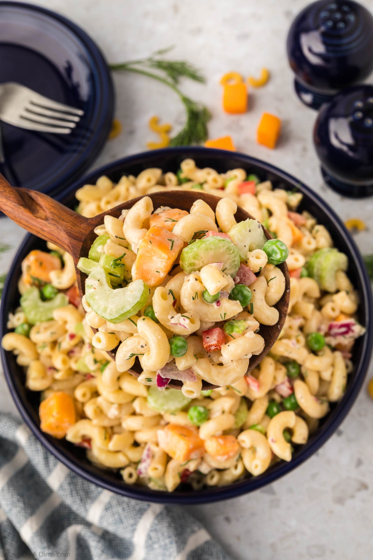 A large spoonful of macaroni salad being scooped out of a large bowl of macaroni salad. 
