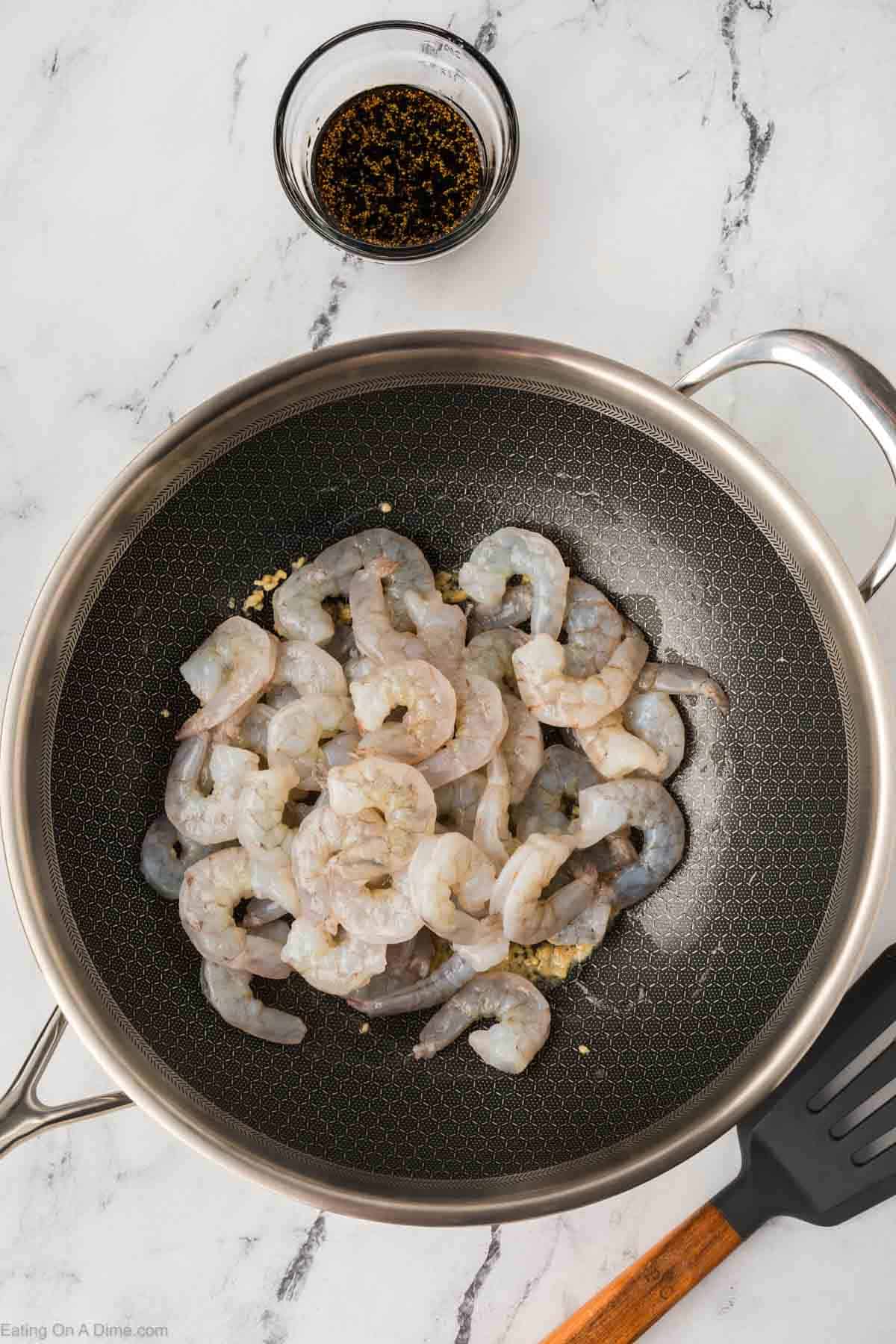 Cooking shrimp in a large skillet with a small bowl of sauce on the side