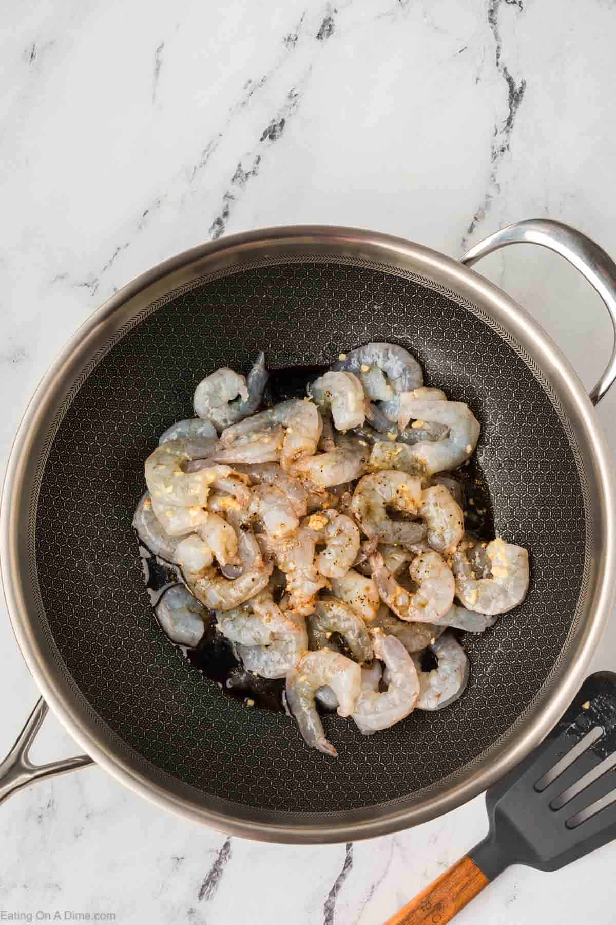 Cooking shrimp topped with minced garlic and sauce in a skillet